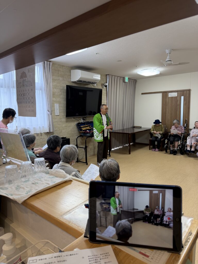 介護施設でのレクリエーション。スタッフが緑色の衣装で入居者に向けて活動を行っている。